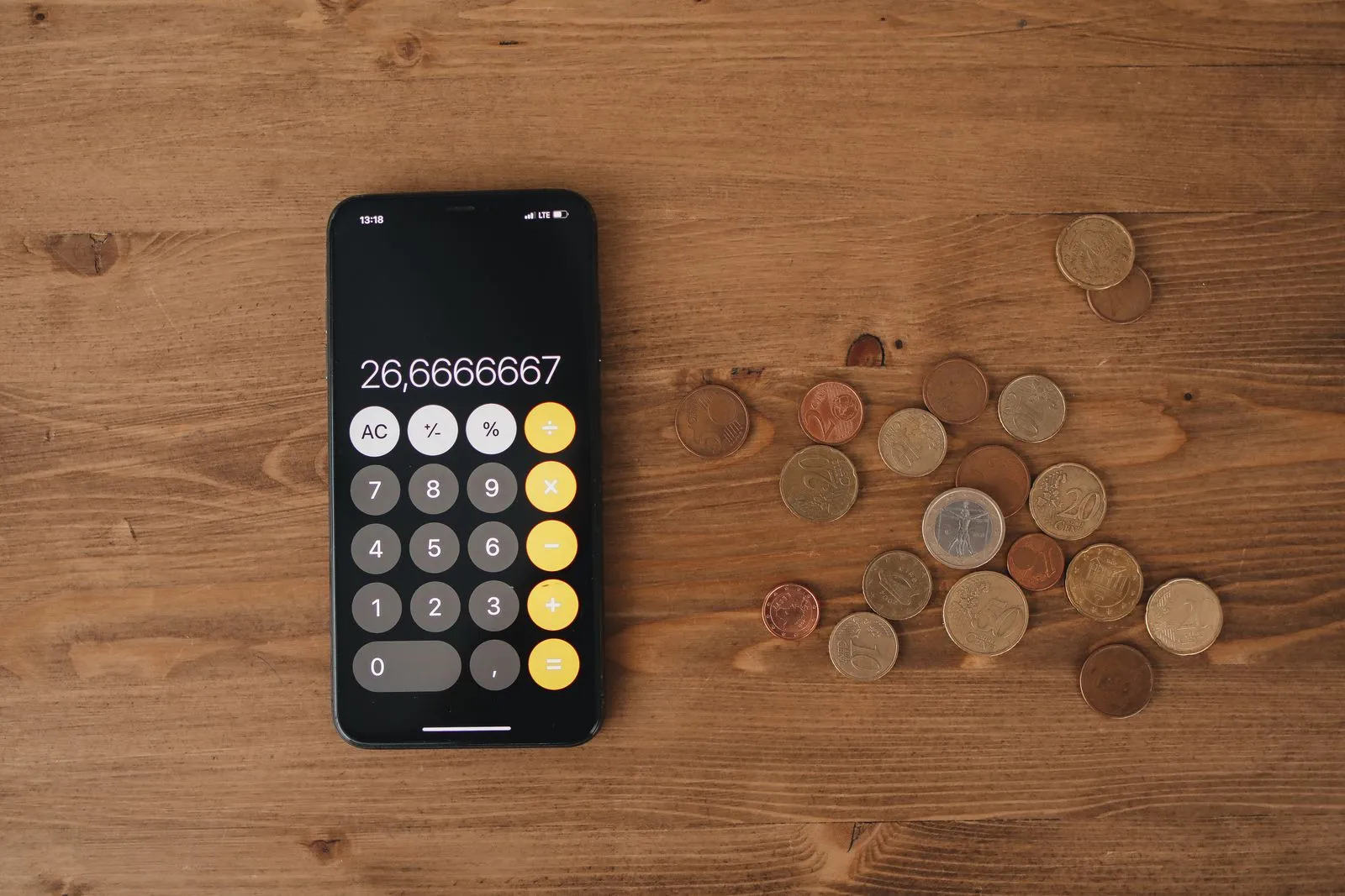 Calculatrice d’un smartphone et pièces en euros sur une table en bois