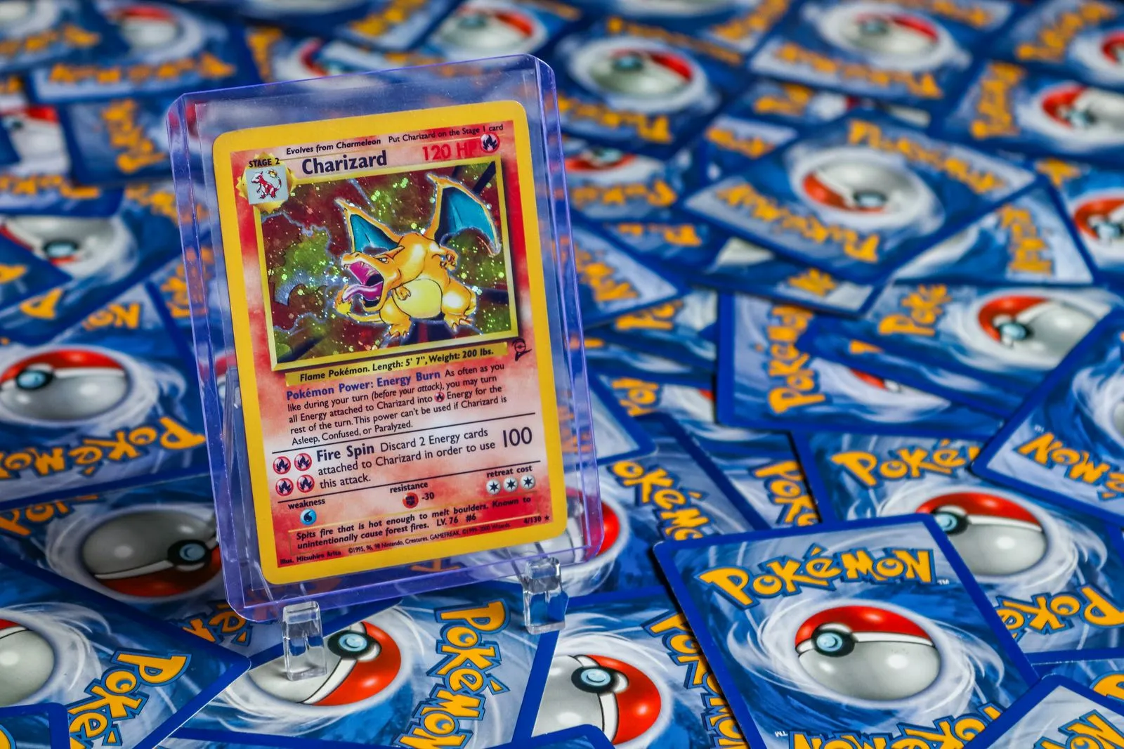 Dracaufeu holographique de Base Set 2, édition anglaise, dans un toploader rigide posé sur un support, au milieu de dos de cartes
